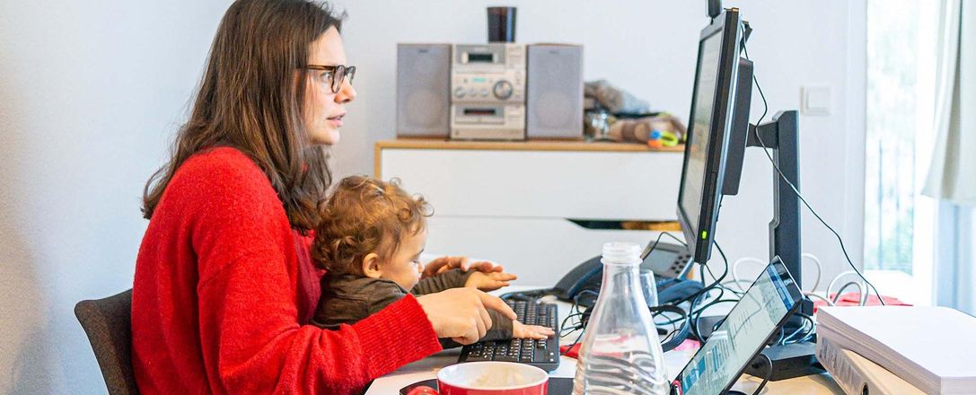Eine Mutter sitzt mit ihrem Kind auf dem Schoß am Schreibtisch vor einem Computer